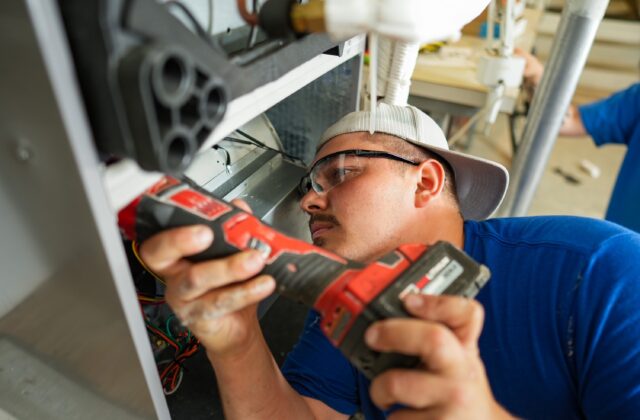 Contractor using a red power tool to install a heat pump